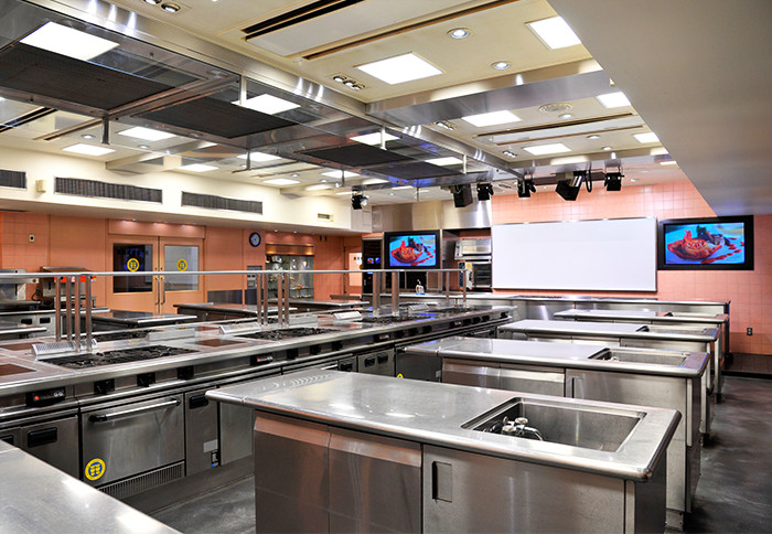 第１調理実習室(本校舎 1F)：西洋料理専用に使われる第1調理実習室。広い室内でも講師の細かい作業をとらえられるよう大型のモニターが設置されています。