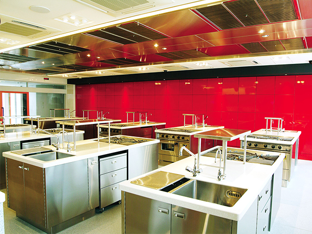 第7・8調理実習室(別館 ANNEXE 4F-5F)：最新の換気天井システムを採用し、厨房をより広く効果的に使用可能に。室内は明るく天井の高い快適な設計。 赤い壁面は収納スペース